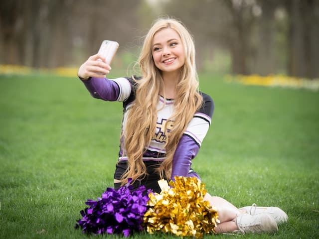cheerleader sitting on the ground taking a picture for snapchat.