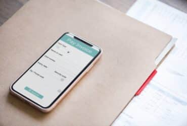 mobile phone displaying an invoice and sitting on top of a folder on a desk