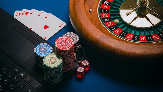 roulette table, cards, dice, and poker chips staked around and on a laptop