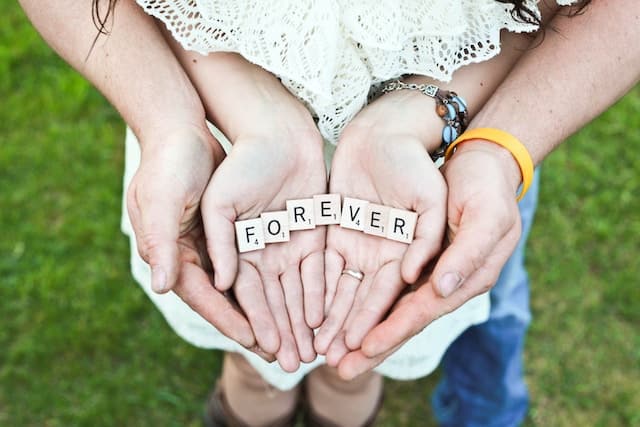 a woman's hands open and sitting on top of a man's open hands. the word forever is spelled with wooden block letters in her hands
