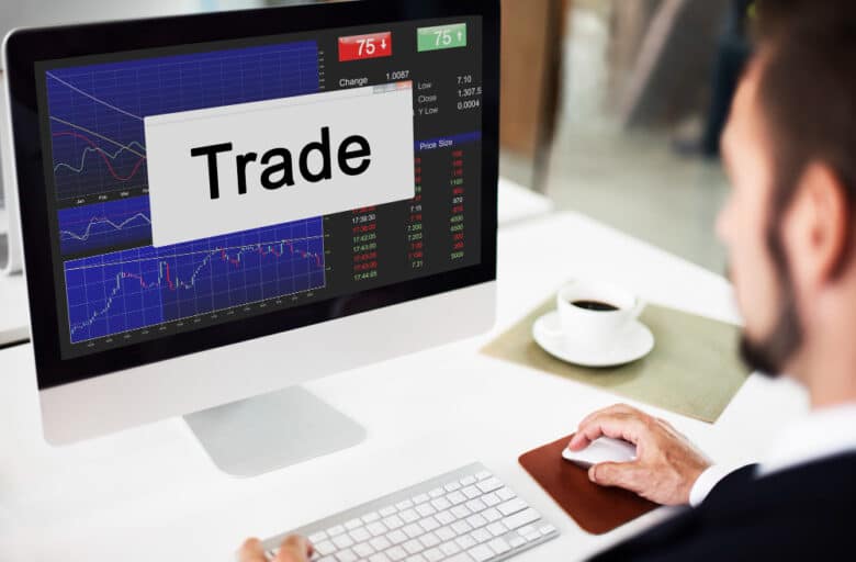 a man sitting at his computer looking at stock quotes, with the word "trade" on his screen