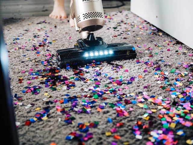 person vacuuming a rug that is covered with confetti from a party