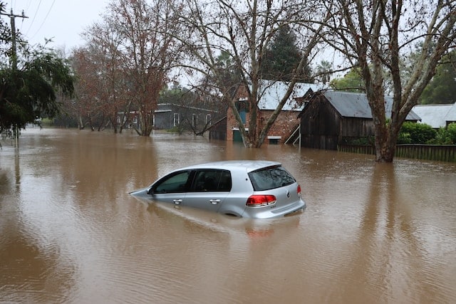flooded street with a car half-submerged under water and houses flooded