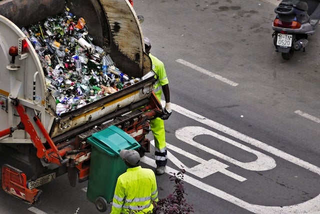 garbage truck with two garbage collectors loading trash bins into it