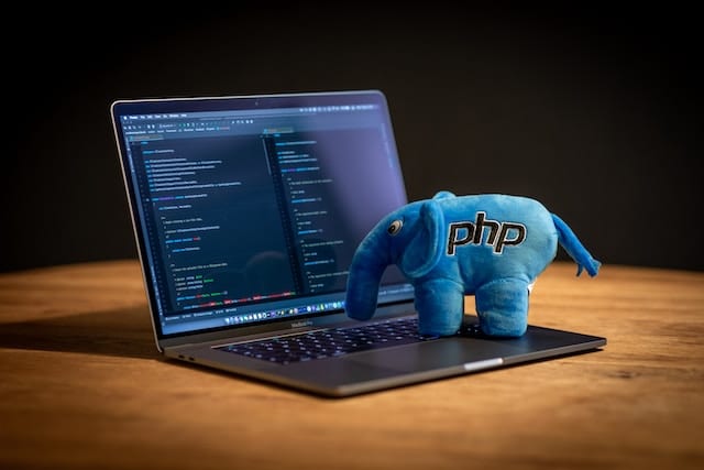 laptop with a blue, plush elephant with the label PHP on it.