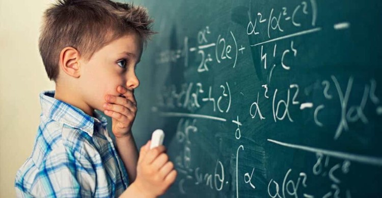 boy thinking about a math problem while at a chalkboard