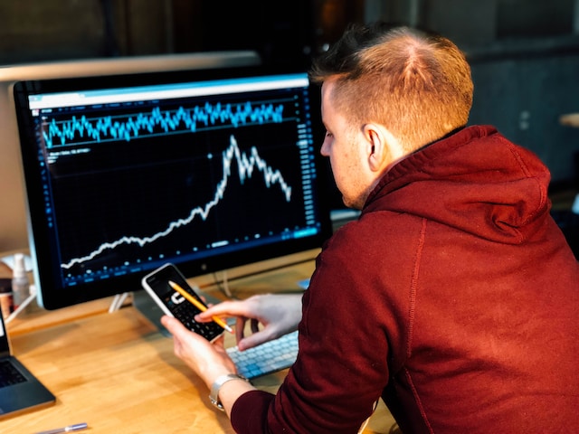 a young man studying his investments on both a smartphone and computer