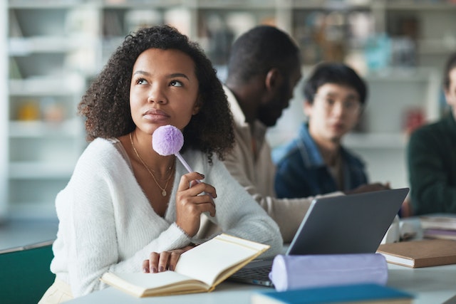 young woman in a white sweater thinking about what to write in a notebook