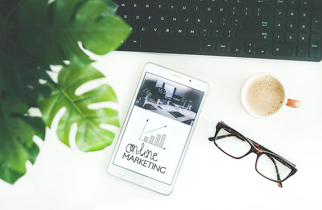 tablet on a desk next to glasses and a keyboard. Tablet says online marketing