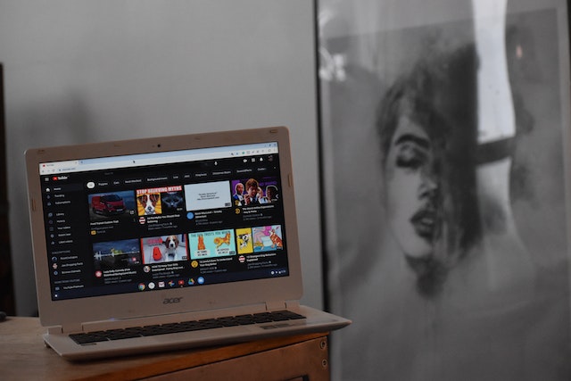 laptop open with YouTube showing. Next to the desk with the laptop is a drawing of a woman's face