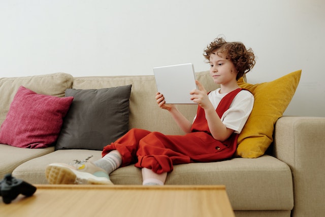 young girl siting on a couch while playing on a tablet