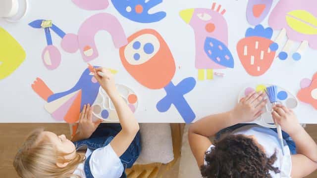 Two girls making a big poster showing birds and fruit