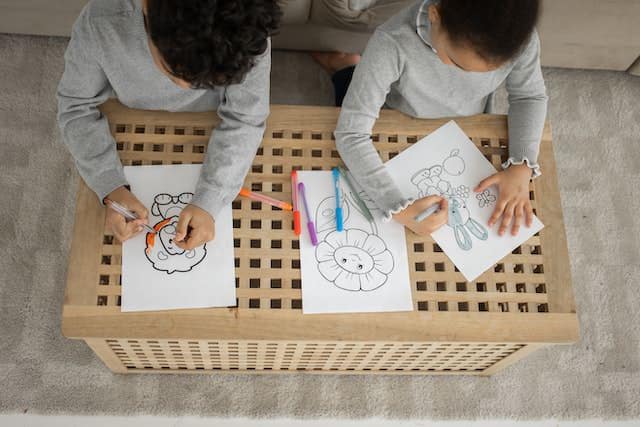 Two boys coloring pictures on a small wooden table