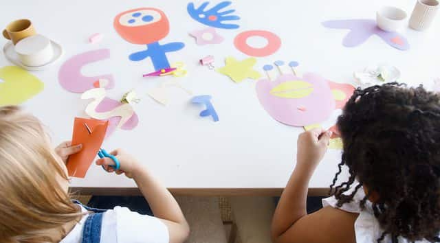 girls cutting out shapes to glue onto a large poster