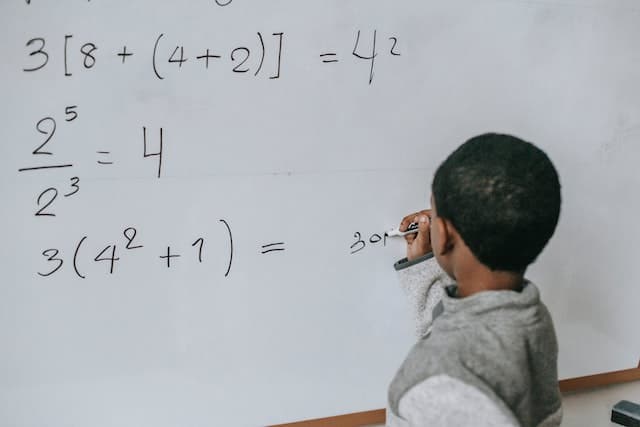 a boy doing math on a white board
