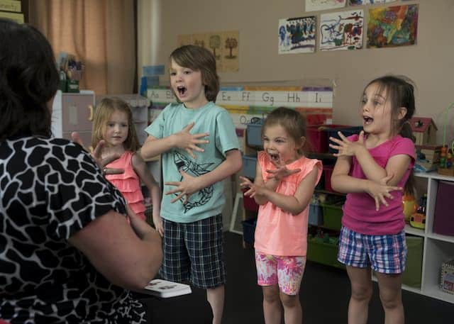 a group of young children singing a song with motions in a class