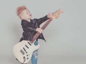 a young boy in a leather jacket holding an electric guitar that is too big for him