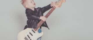 a young boy in a leather jacket holding an electric guitar that is too big for him