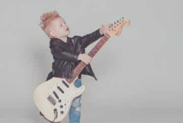 a young boy in a leather jacket holding an electric guitar that is too big for him