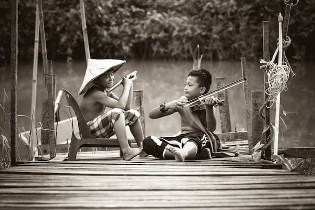 two Asian boys sitting on a dock, playing musical instruments together