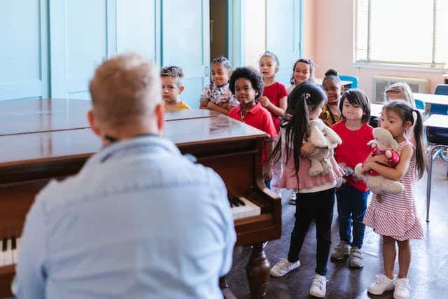music teacher sitting at a piano while teaching a group of young children
