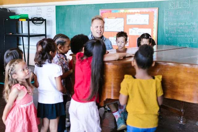 Children singing in music class while teacher plays the piano