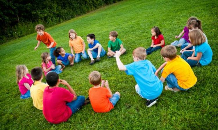 a group of children playing duck duck goose on a lawn.