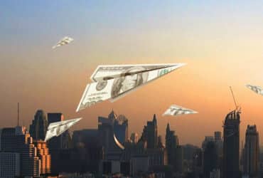 dollar bills folded into paper airplanes and flying above city skyline