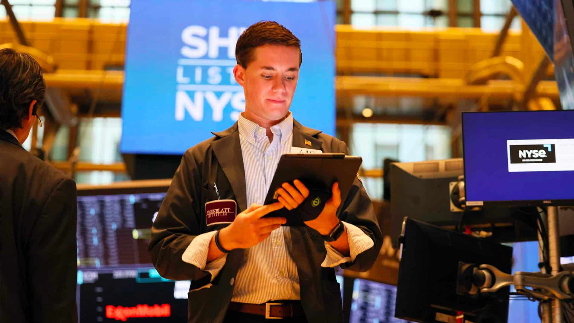 man standing on stock exchange floor looking at a tablet