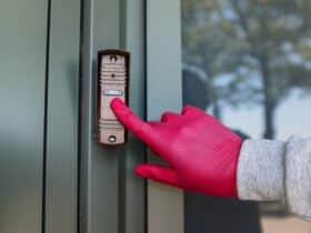 man in a grey sweatshirt and red gloves ringing a doorbell.