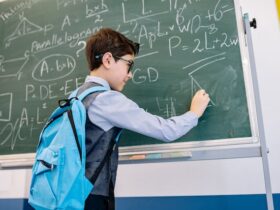 Boy wearing backpack working complex math problems on a chalkboard.