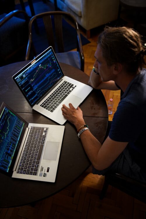 man working on data analysis on two laptops.
