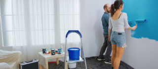 young couple painting a living room wall with rollers.