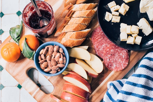 a variety of meat, cheese, fruit, and nuts on a cutting board.