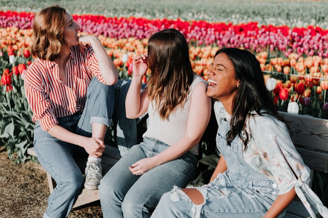 three women sitting on a bench with a tulip field behind them.