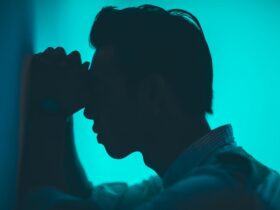 young man in pain leaning against a wall.