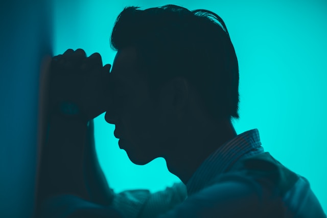 young man in pain leaning against a wall.