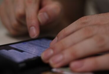 closeup of a man's hands reviewing texts on his phone.