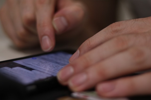 closeup of a man's hands reviewing texts on his phone.