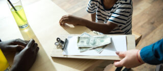 clipboard with money and paper on it and little kid looking up at person holding it