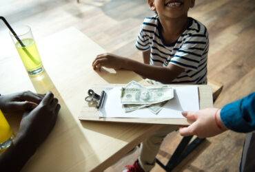 clipboard with money and paper on it and little kid looking up at person holding it