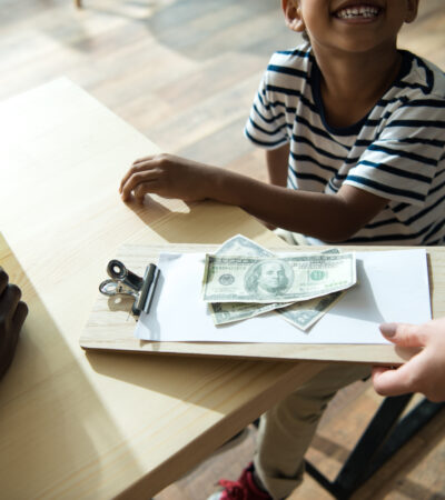 clipboard with money and paper on it and little kid looking up at person holding it