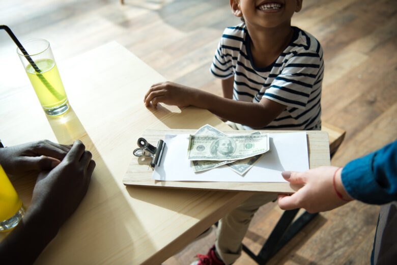 clipboard with money and paper on it and little kid looking up at person holding it