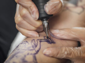 Hand of tattooist in rubber gloves drawing a tattoo with electric tattoo gun, close-up